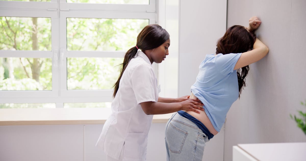A pregnant woman receiving gentle chiropractic care in a clinic setting, side-lying on a treatment table