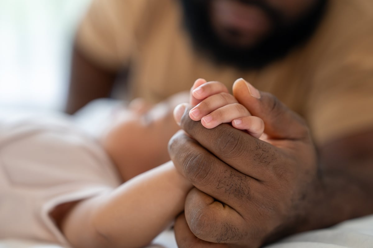 A parent gently holding their newborn baby's hand while resting together
