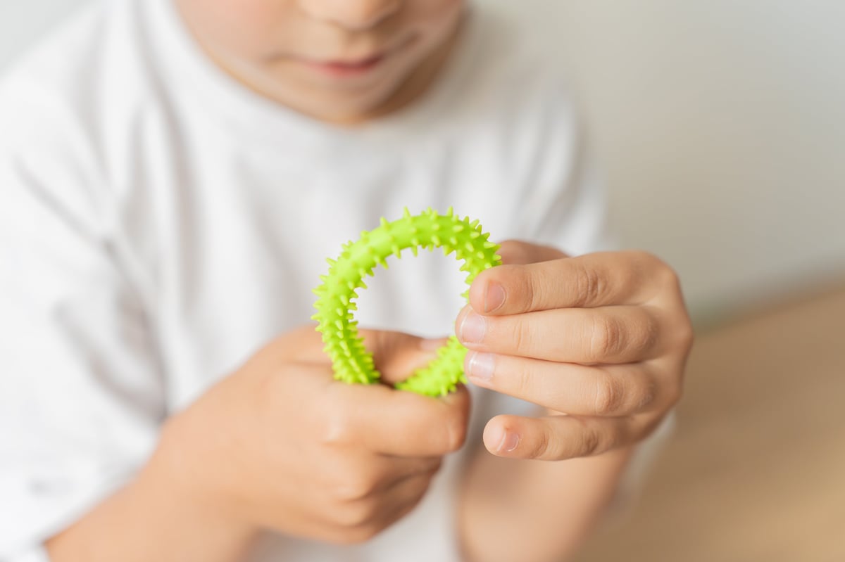 Close up of child hands touching a textured green sensory toy, concept of tactile exploration and motor skills.