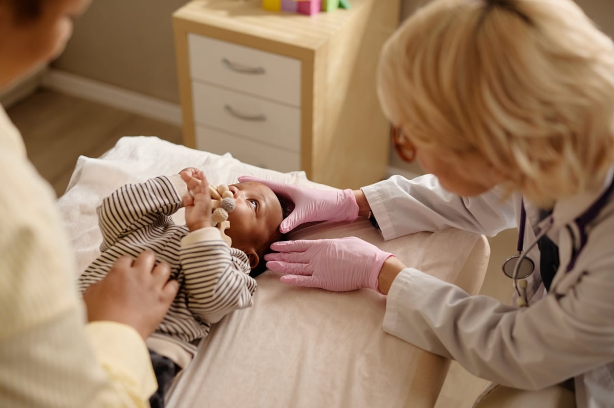Pediatrician examining infant during checkup while mother supporting child in clinic, showing preventive healthcare and pediatric care.